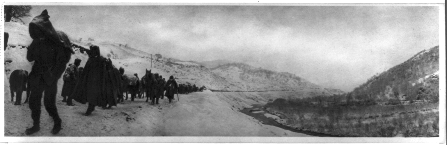 Photograph shows people and horses marching along a snowy road, probably in Albani, curving through a wintry valley.